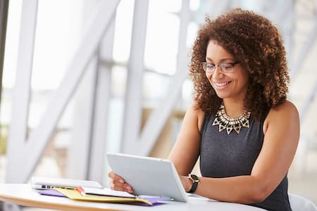 Young woman with curly hair, wearing glasses, smiling at a tablet screen